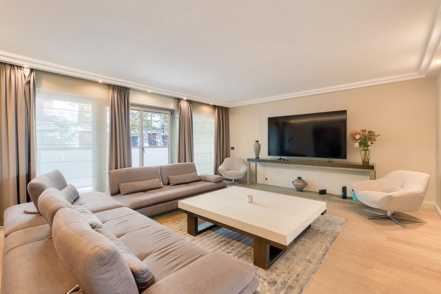 Een moderne woonkamer met een zithoek, een salontafel en een flatscreen televisie aan de muur.