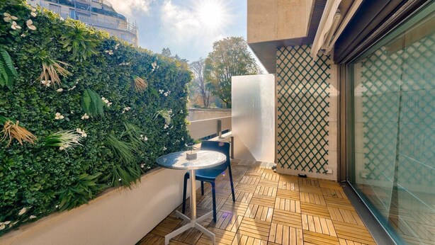 A modern outdoor seating area with a wooden floor, a round table, and chairs, surrounded by a green vertical garden and a glass partition. - Prestigious 5BR Avenue Foch Home - Arc de Triomphe (Paris)