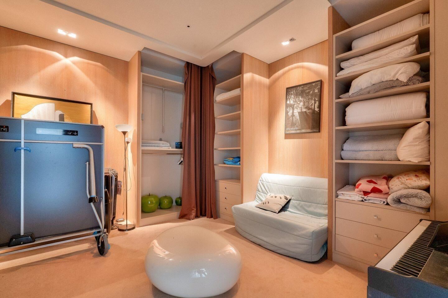 A modern bedroom with a built-in wardrobe, a seating area with a sofa, and a large white ottoman.
