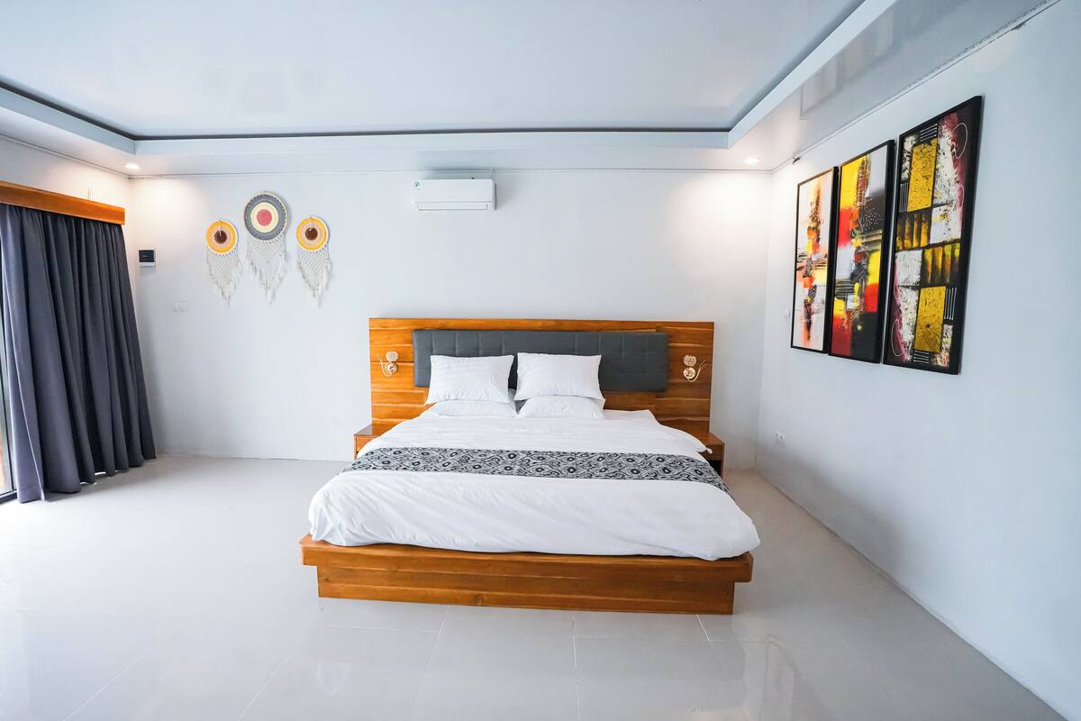 A modern bedroom with a wooden bed, white bedding, a grey headboard, and a large window with curtains.