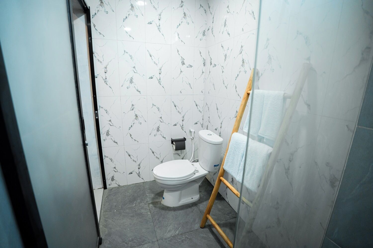 A small, modern bathroom with a toilet, a towel rack, and a wooden ladder.