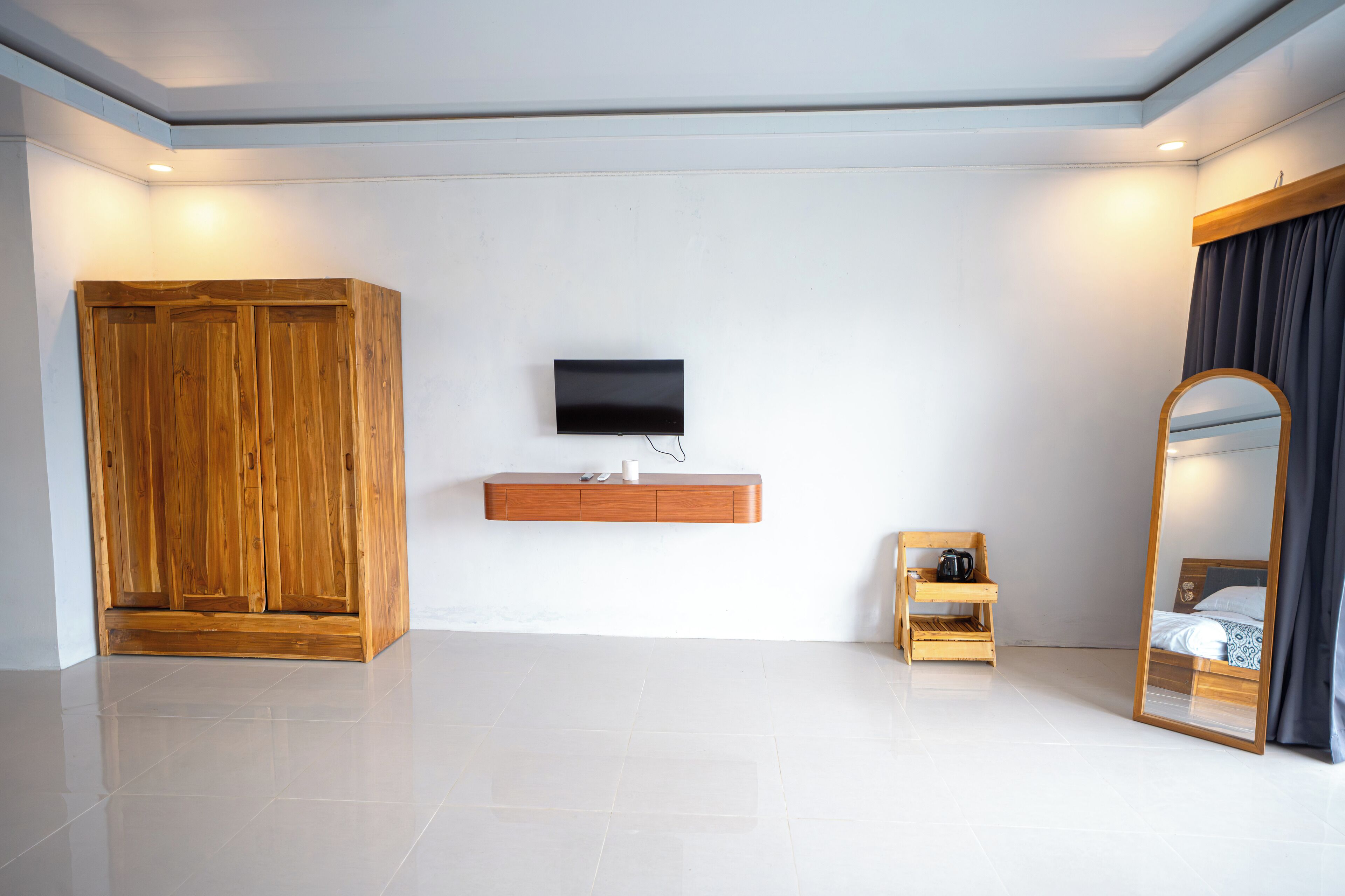 A modern hotel room with a wooden wardrobe, a mounted TV, a small wooden shelf, and a large mirror.