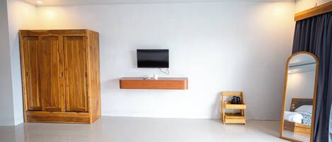 A modern hotel room with a wooden wardrobe, a mounted TV, a small wooden shelf, and a large mirror.