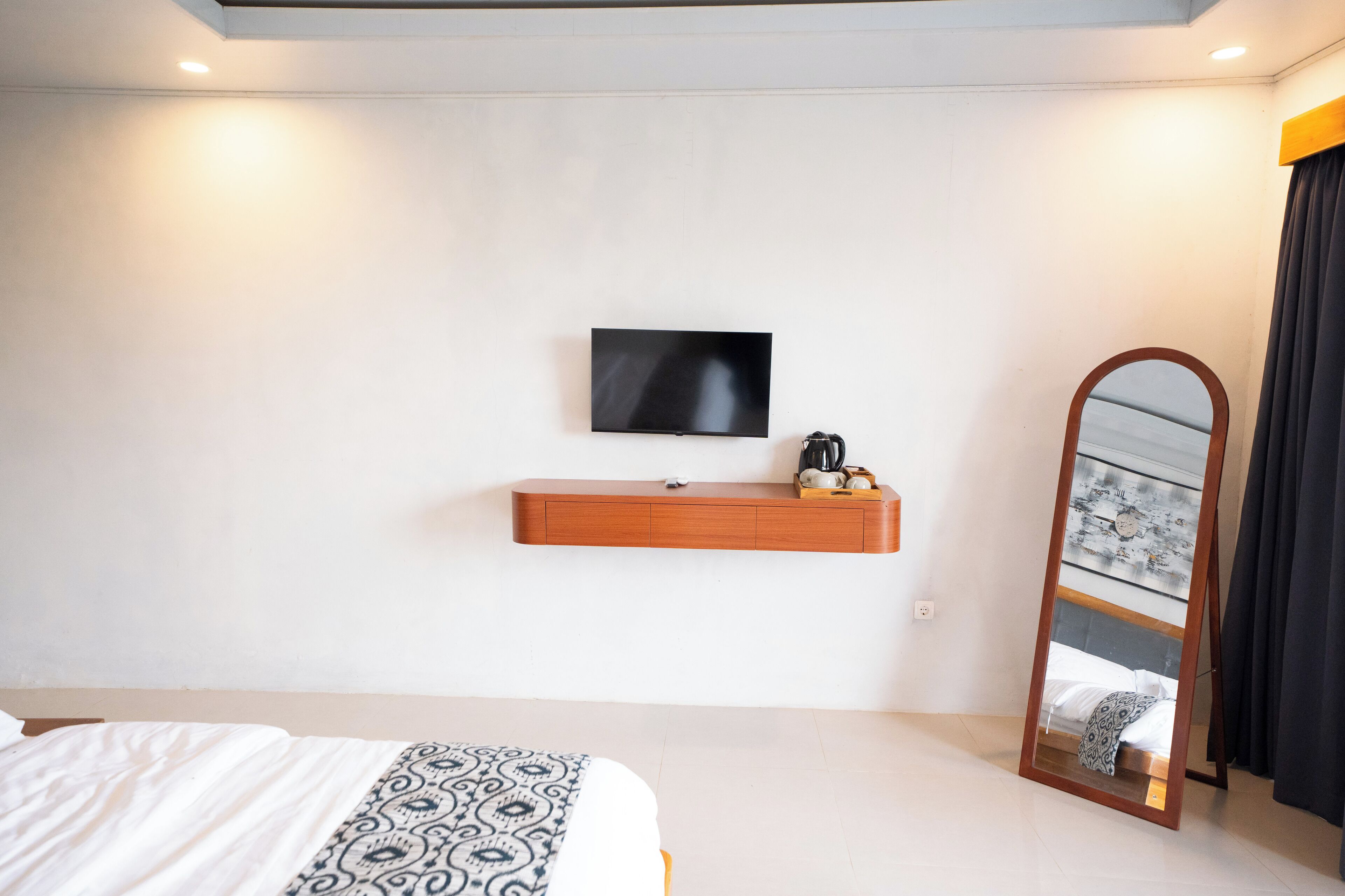 A modern hotel room with a large bed, a mounted TV, a wooden console table with a coffee maker, and a full-length mirror.
