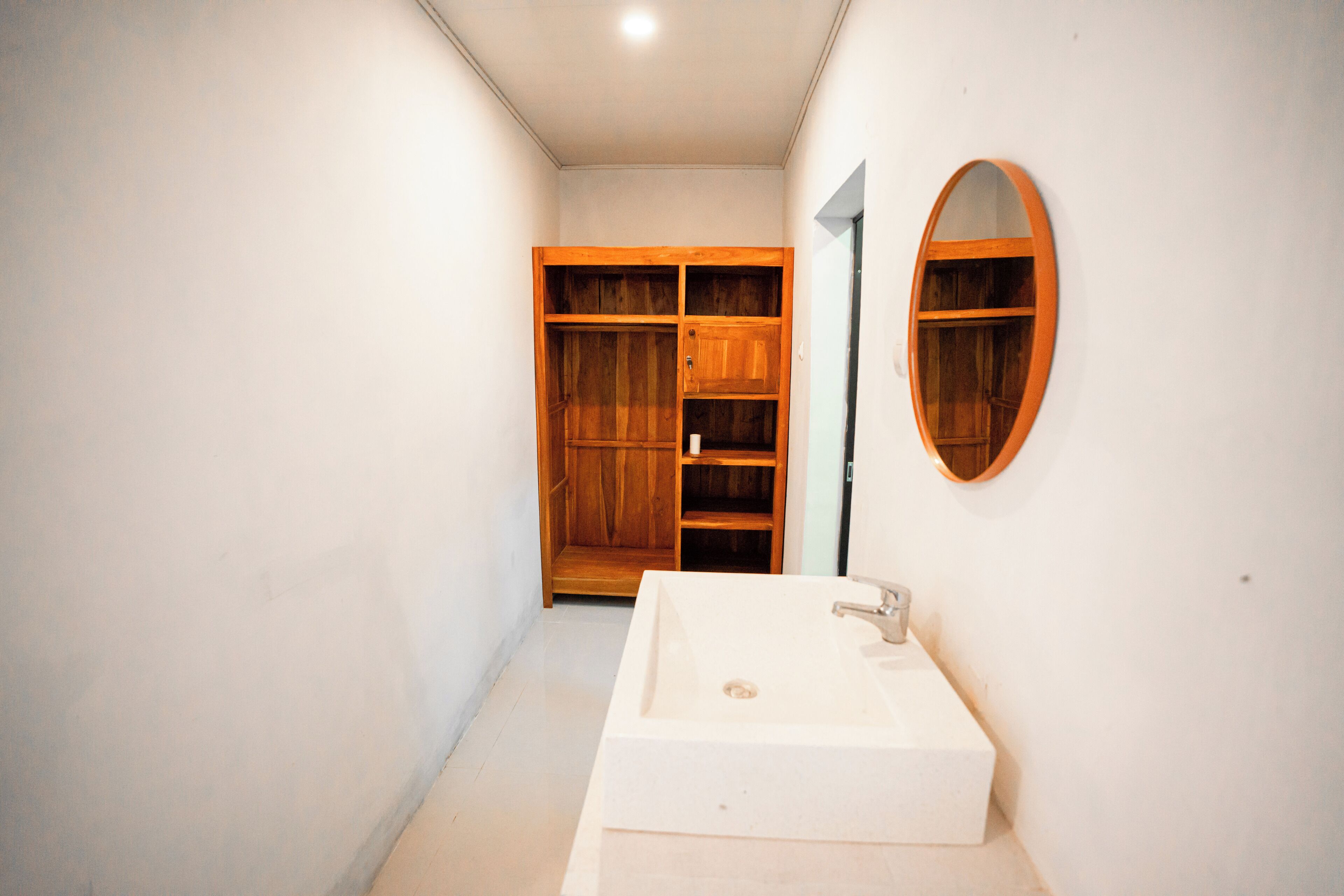 Une salle de bain avec un lavabo blanc, des étagères en bois et un miroir.