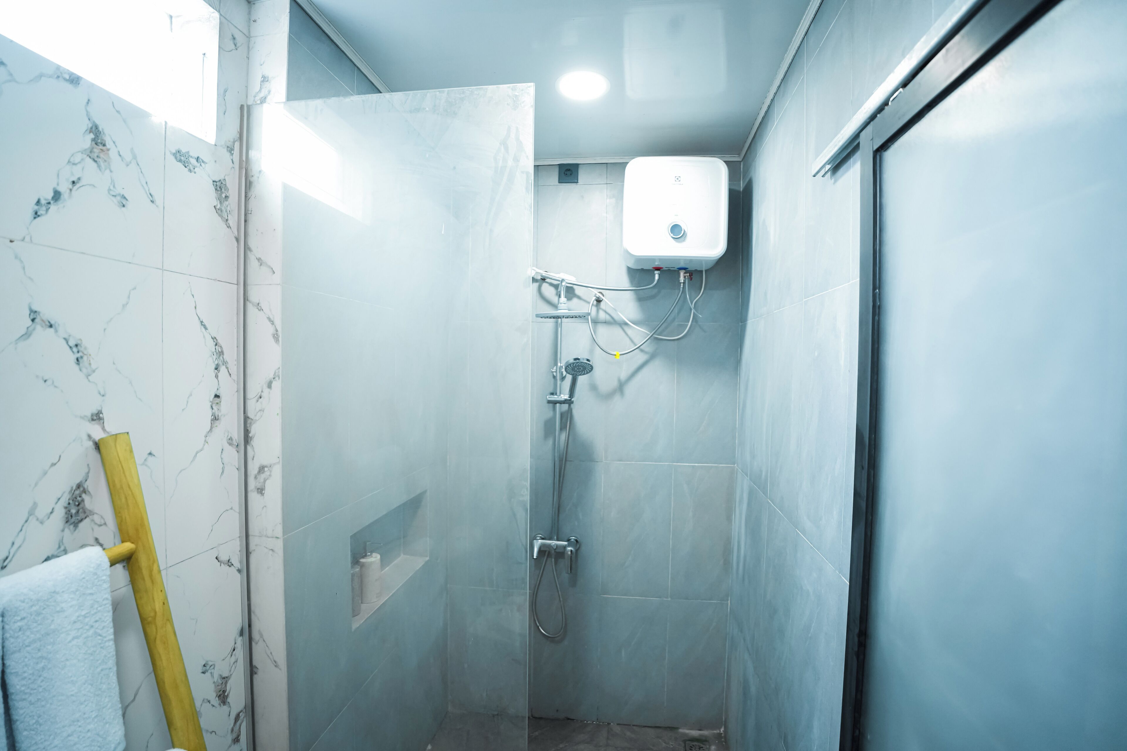 A bathroom with a shower, marble tiles, a towel rack, and a soap dispenser.