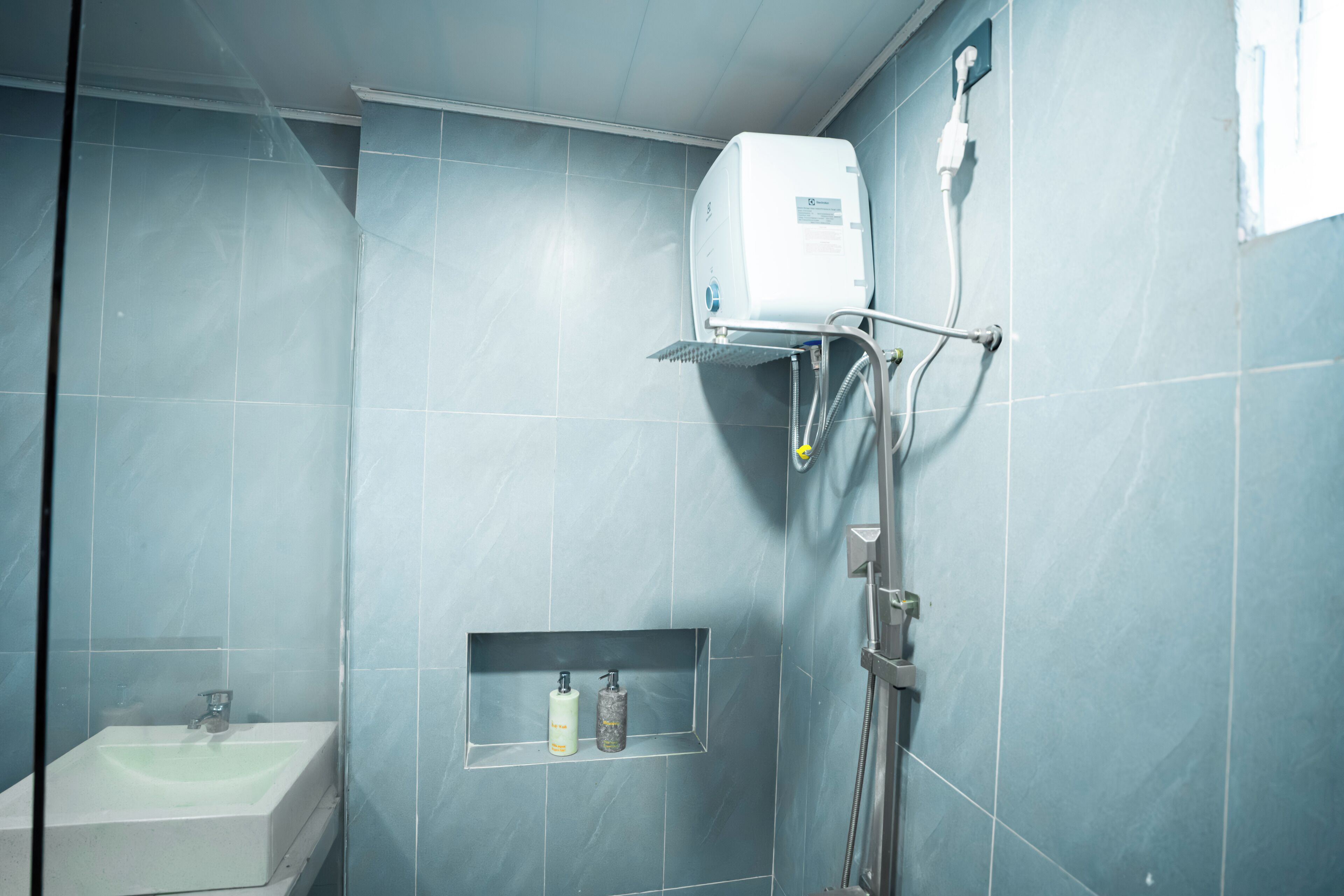 A bathroom with a shower, sink, and storage shelf.