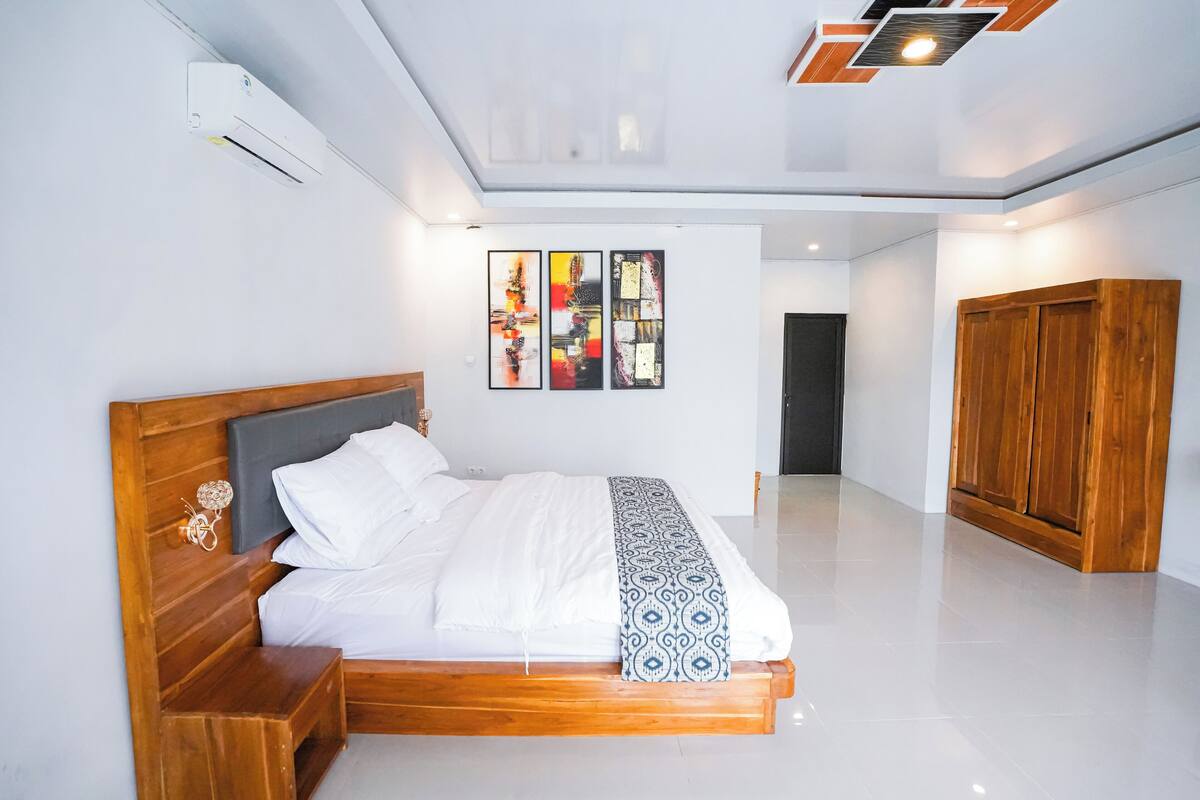 A modern bedroom with a wooden bed, white bedding, and a large artwork on the wall.