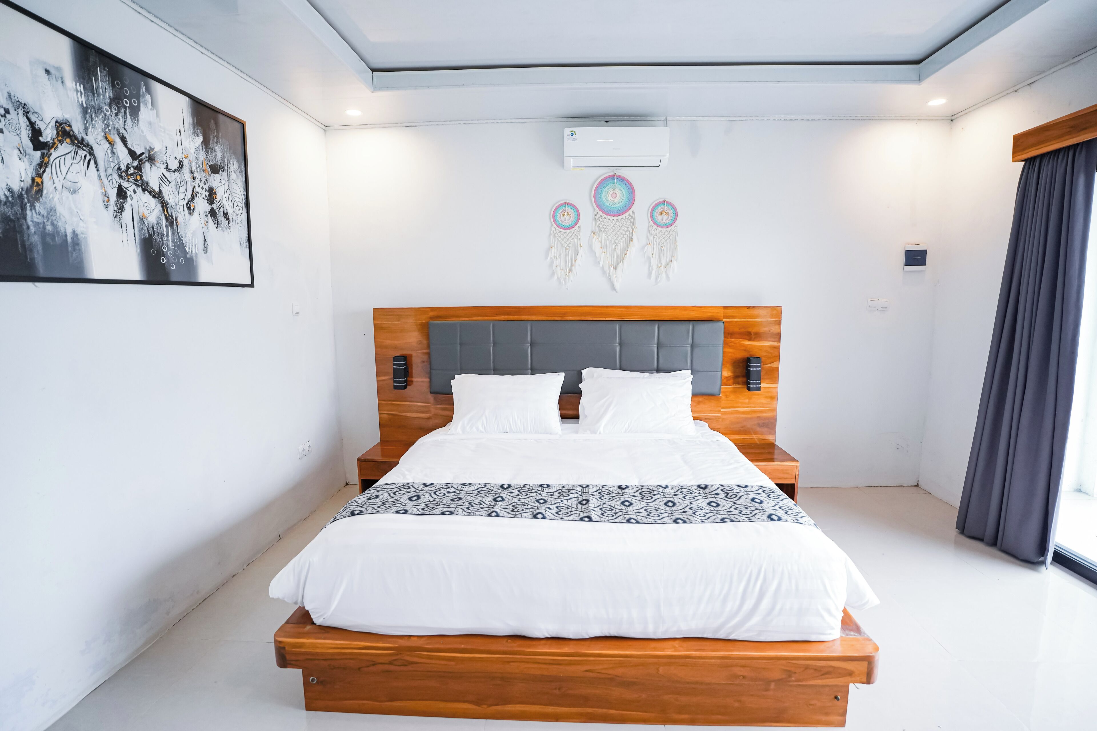 Ein modernes Schlafzimmer mit einem hölzernen Bett, weißer Bettwäsche, einem großen abstrakten Gemälde und dekorativen Wandgestaltungen.