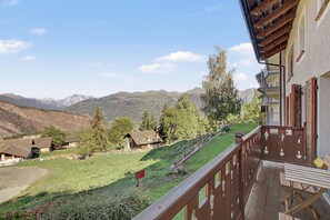 A wooden balcony with a view of a mountainous landscape and traditional houses. - Apartment 'Maison Erica - Ozein' with Mountain View and Private Outdoor Area (Ozein)