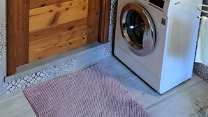 A laundry room with a wooden door, a washing machine, patterned tiles, and a small mirror. - Apartment 'Maison Erica - Ozein' with Mountain View and Private Outdoor Area (Ozein)