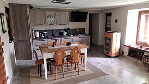 A compact kitchen with wooden cabinets, a dining table with chairs, a built-in oven, and a window. - Apartment 'Maison Erica - Ozein' with Mountain View and Private Outdoor Area (Ozein)