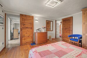 Ein Schlafzimmer mit Holztüren, einem Bett mit einem gemusterten Quilz, einem blauen Stuhl und einer Kommode.