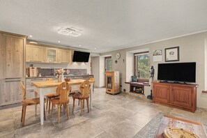 Una cocina moderna con armarios de madera, un comedor con mesa y sillas de madera, horno empotrado y televisor de pantalla plana en la pared.