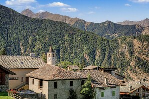 Un pueblo montañoso con edificios de piedra tradicionales, una iglesia con campanario y cielo despejado.
