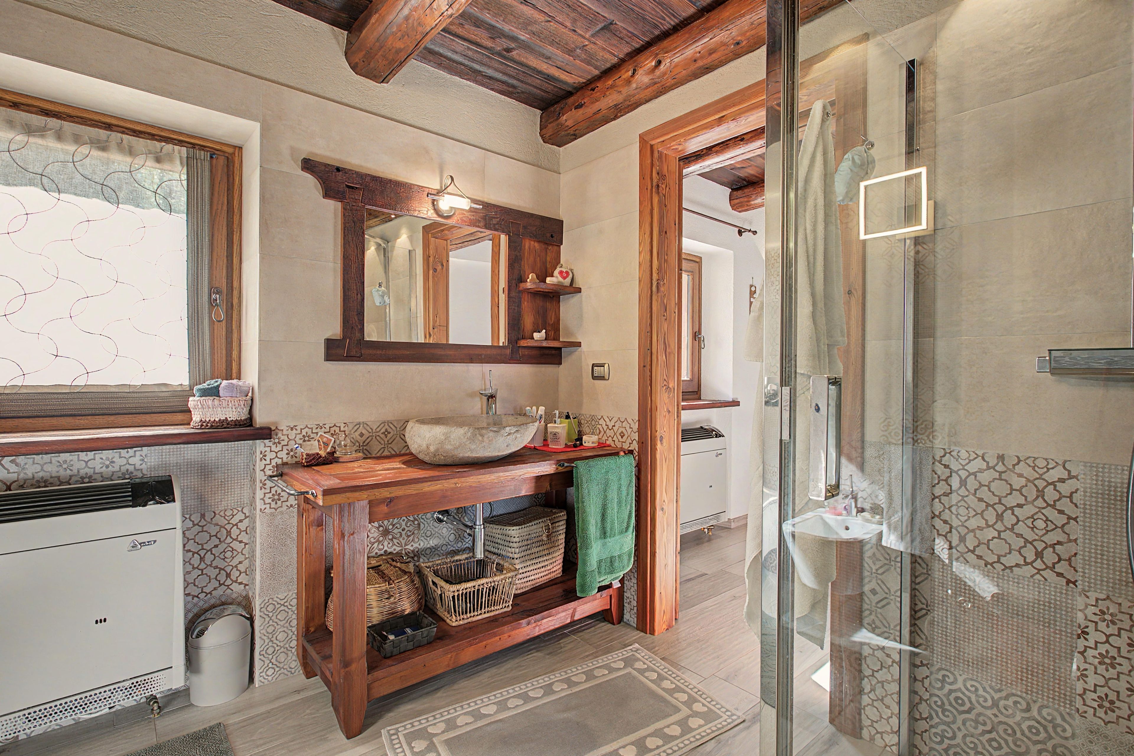 A bathroom with a wooden vanity, a large mirror, a glass shower enclosure, and patterned tiles.