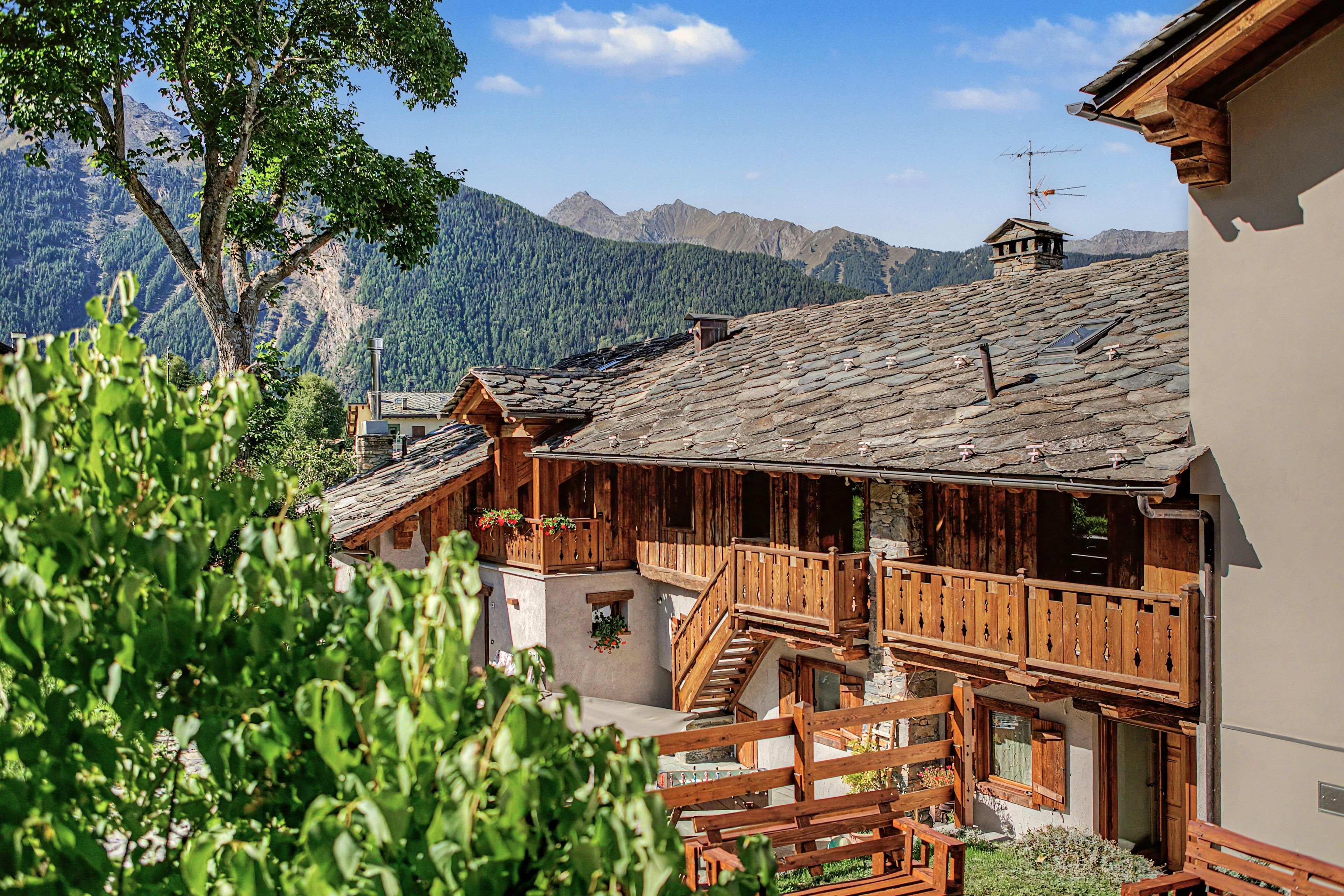 Ein traditionelles Holzchalet mit Steinziegeldach, einer Holzbalkon und Blick auf die umliegenden Berge.