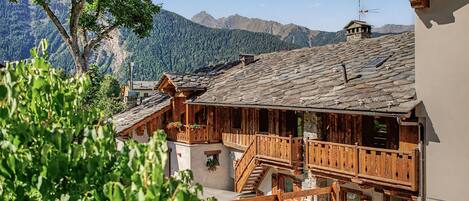 Ein traditionelles Holzchalet mit Steinziegeldach, einer Holzbalkon und Blick auf die umliegenden Berge.