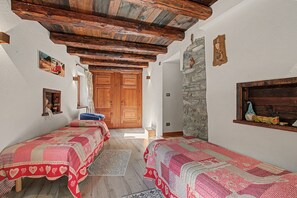 Una habitación con dos camas, vigas de madera, una pared de piedra y una puerta de madera.