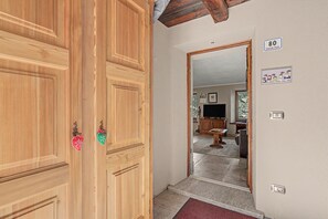 A wooden door with a mirror reflecting a living room with a TV, a wooden cabinet, and a window. - Apartment 'Maison Erica - Ozein' with Mountain View and Private Outdoor Area (Ozein)