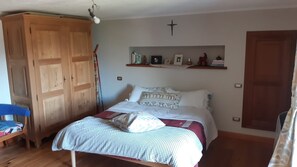 A bedroom with a bed, wooden wardrobe, shelf with decorations, and a cross on the wall.