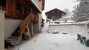 Ein verschneiter Außenbereich mit Holzstufen, die zu einem Gebäude führen, einer Steinmauer und einem Holzzaun.
