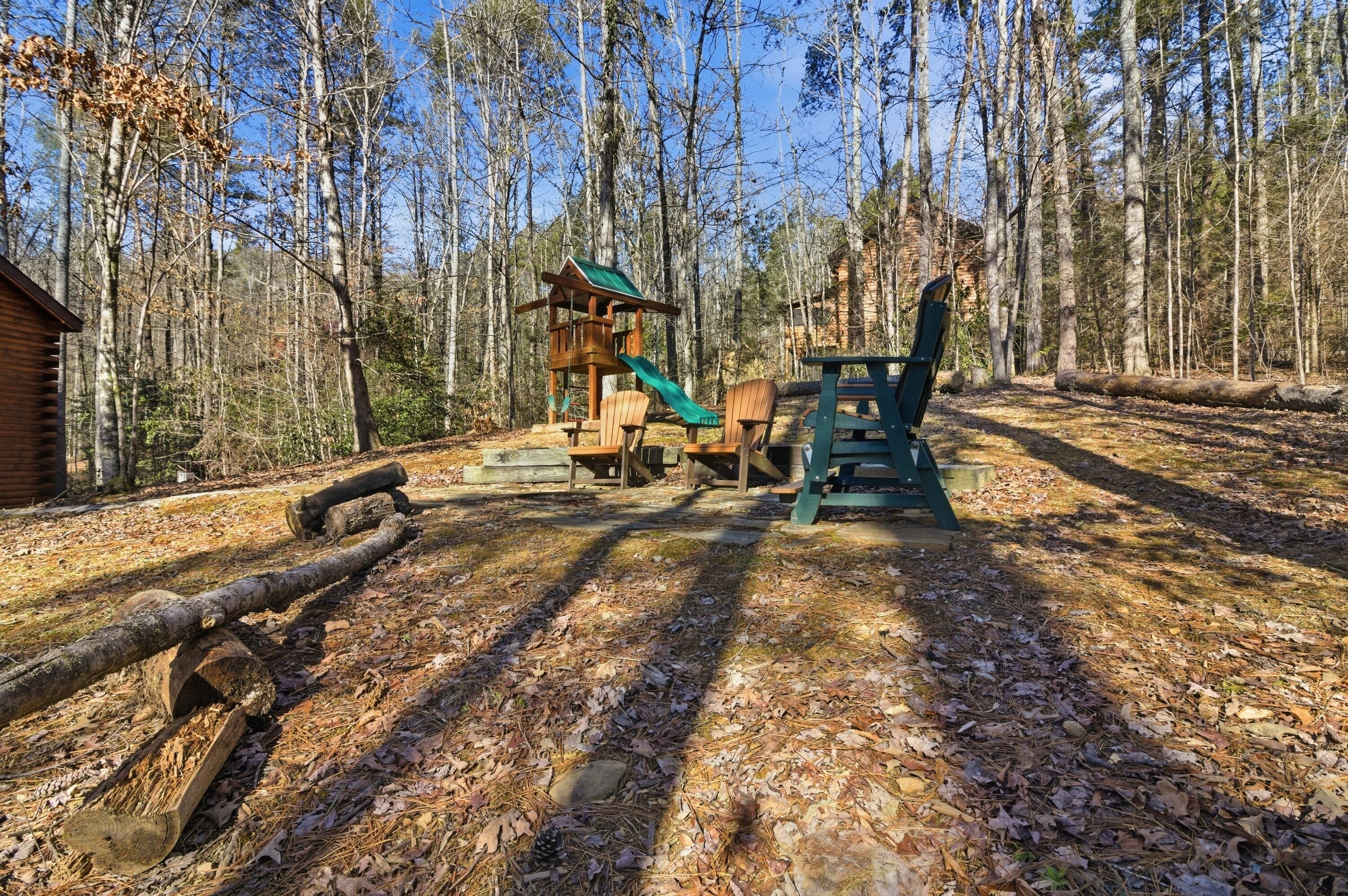 A wooden play structure with a slide and a picnic table in a forested area.