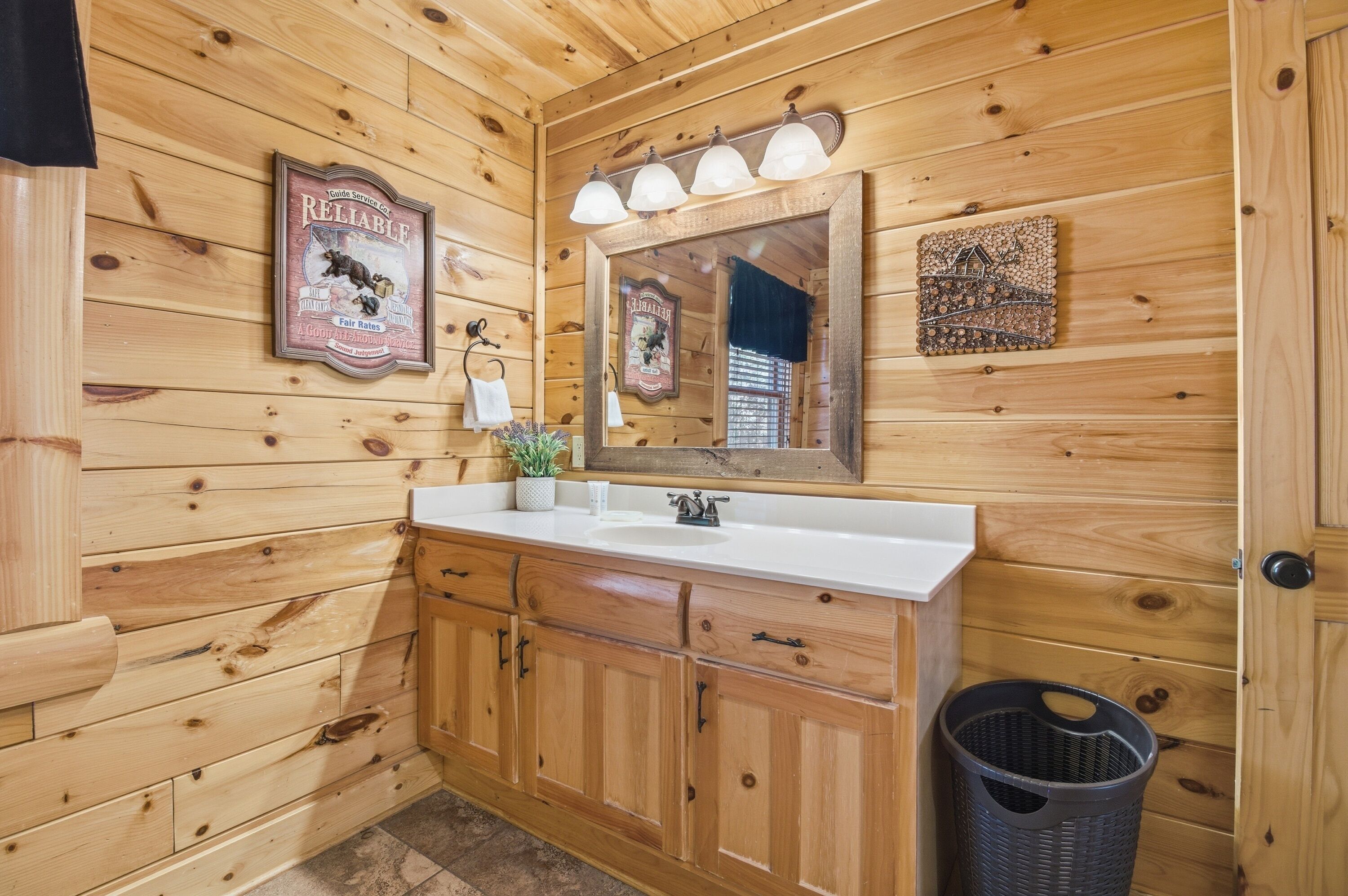 A wooden cabin bathroom with a white sink, wooden cabinets, a mirror, and a framed picture on the wall.