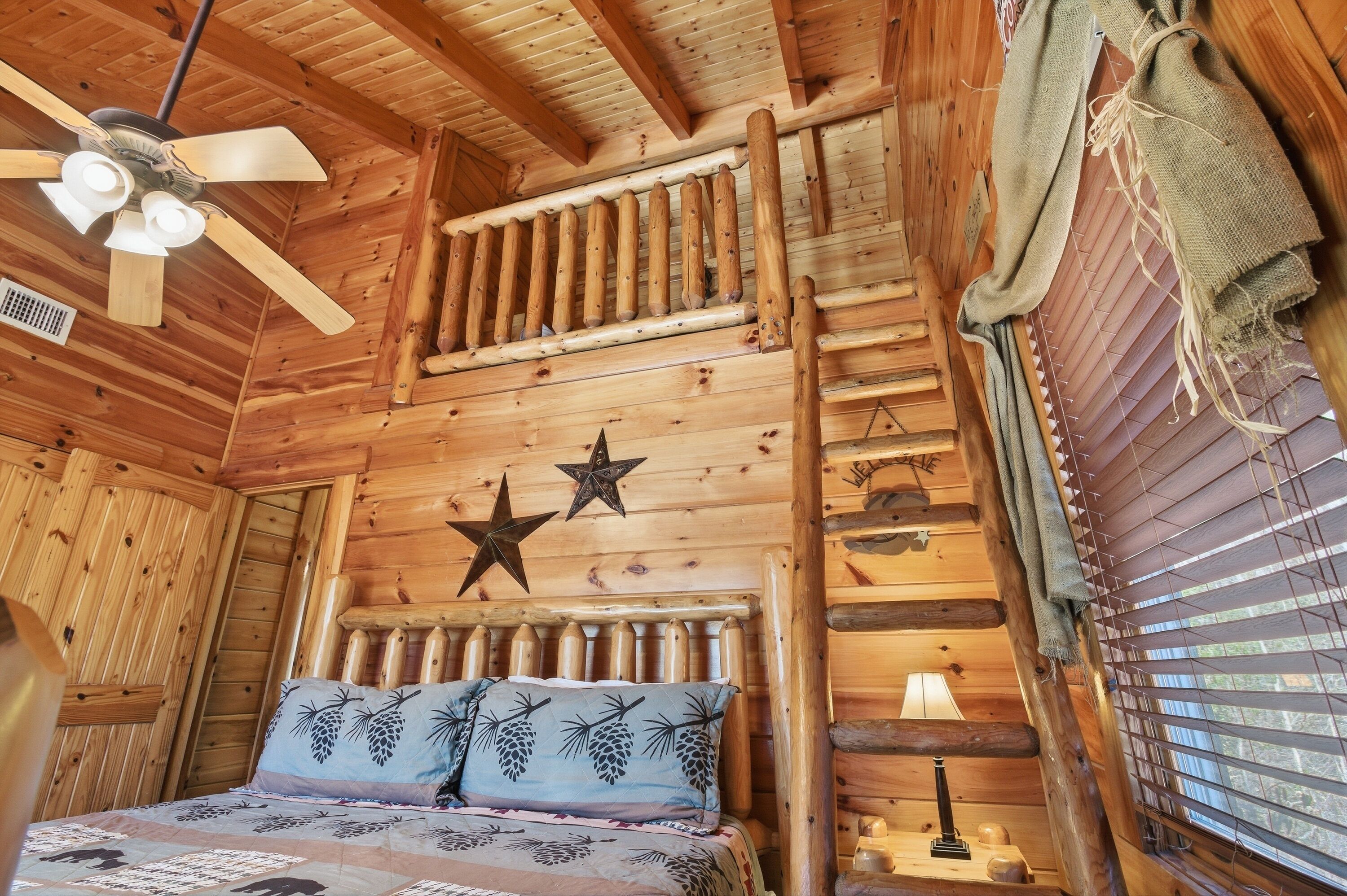 A wooden cabin room with a bed, a ceiling fan, a star decoration, and a window with blinds.