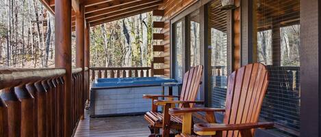 A wooden deck with a hot tub, wooden chairs, and a view of trees.