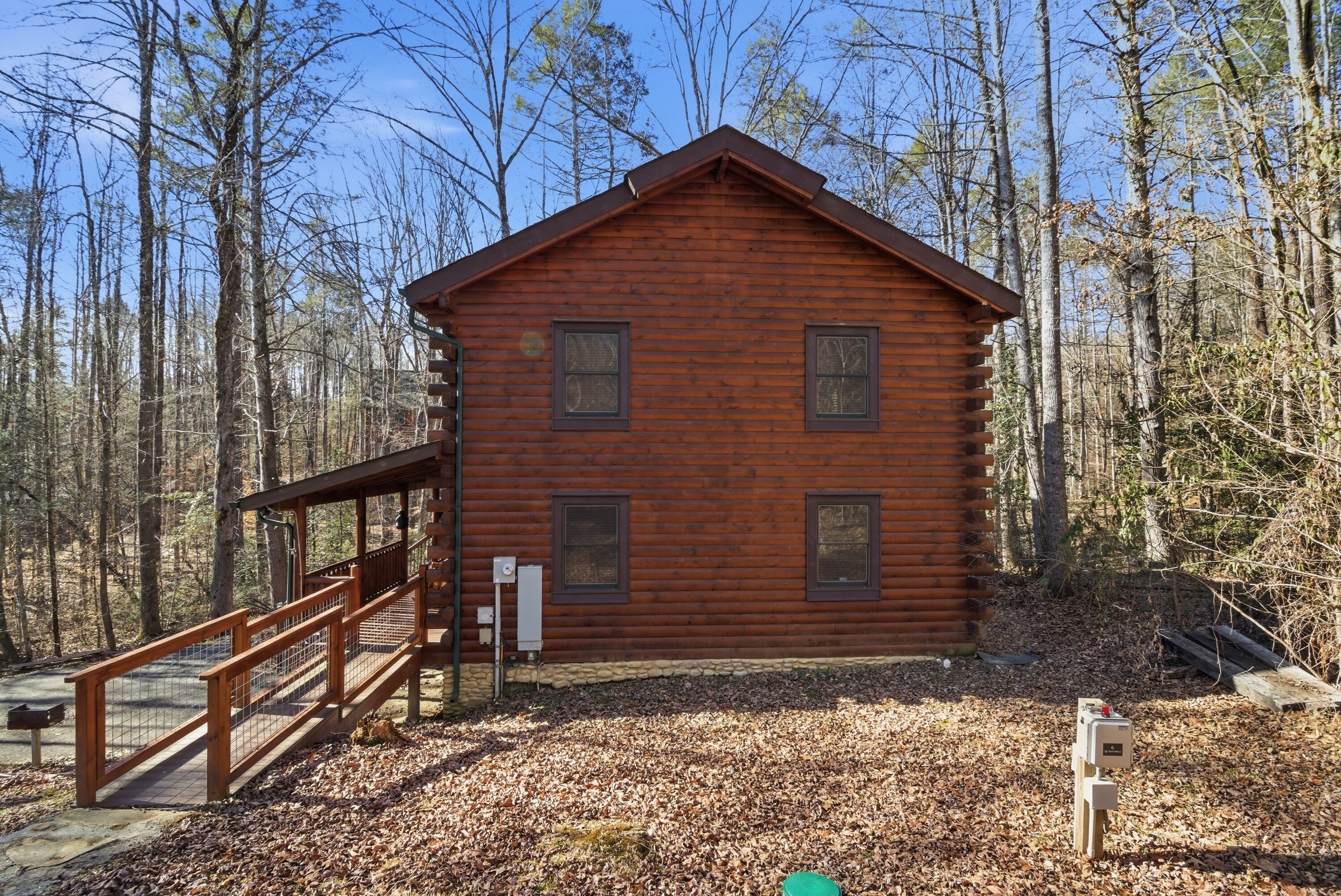 A wooden cabin with a wooden deck and a metal railing, surrounded by trees.