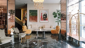 A lobby with a sofa, chairs, a coffee table, a chandelier, artwork, and a plant.