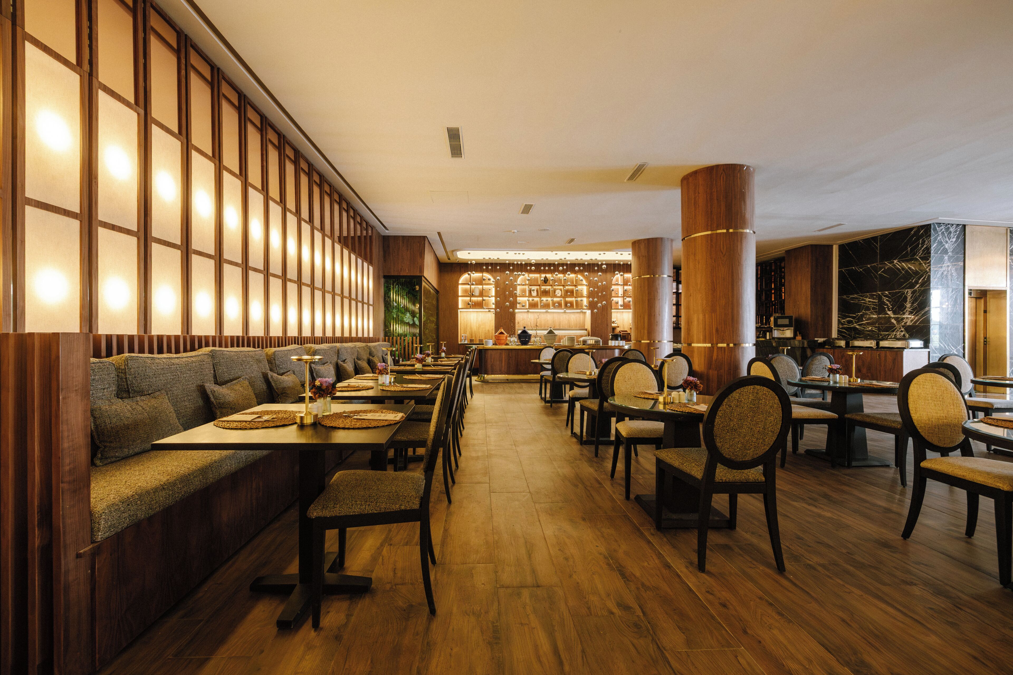 A restaurant with wooden flooring, high-backed chairs, and a long counter.
