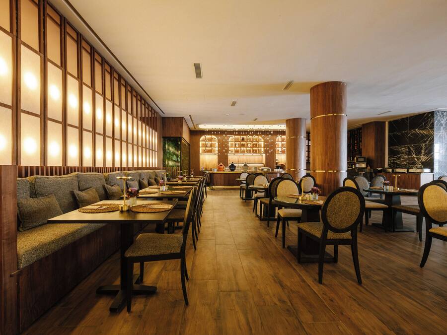 A restaurant with wooden flooring, high-backed chairs, and a long counter.