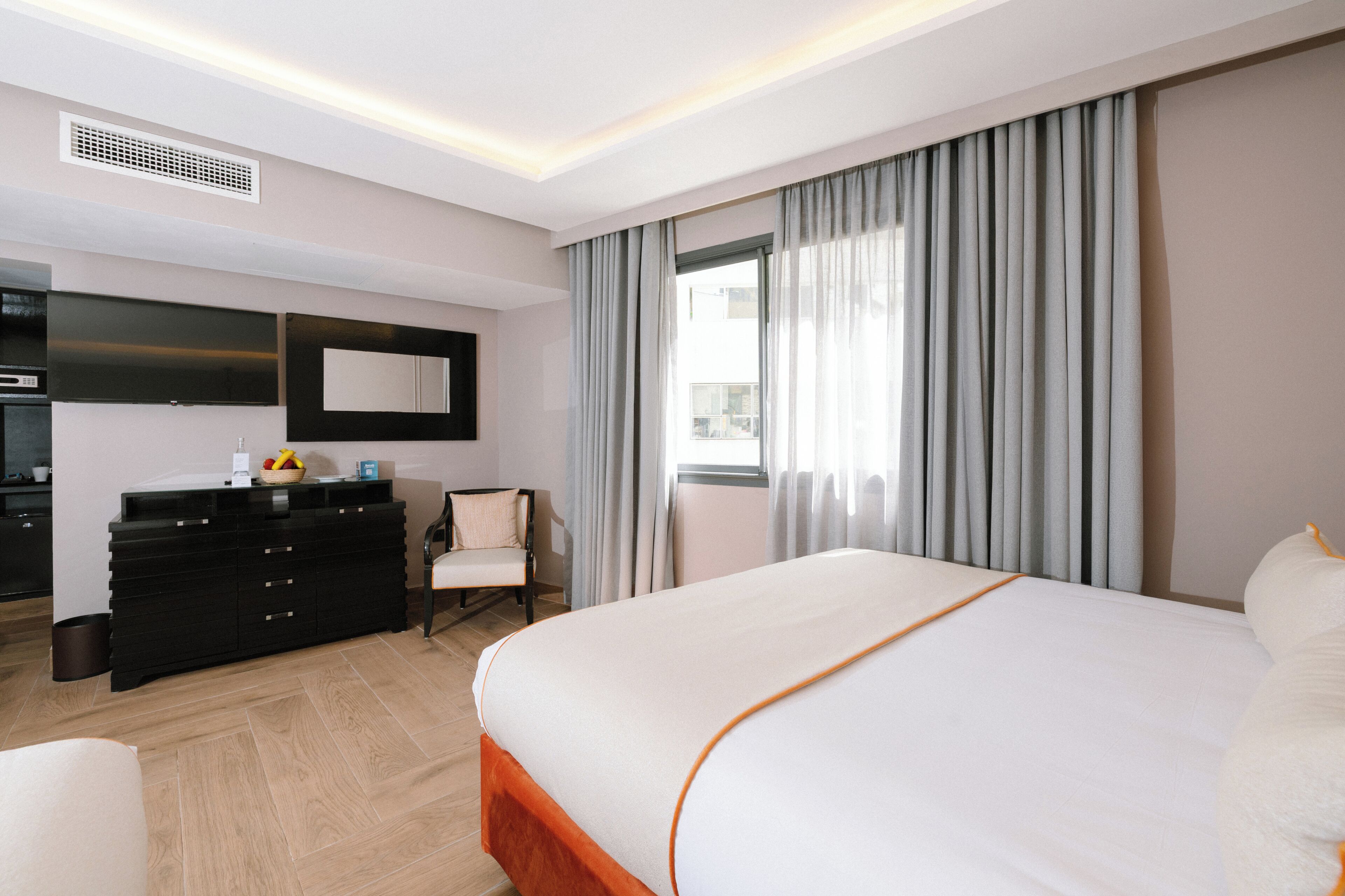 A hotel room with a bed, a dresser, a chair, a TV, and a window with curtains.