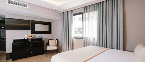 A hotel room with a bed, a dresser, a chair, a TV, and a window with curtains.