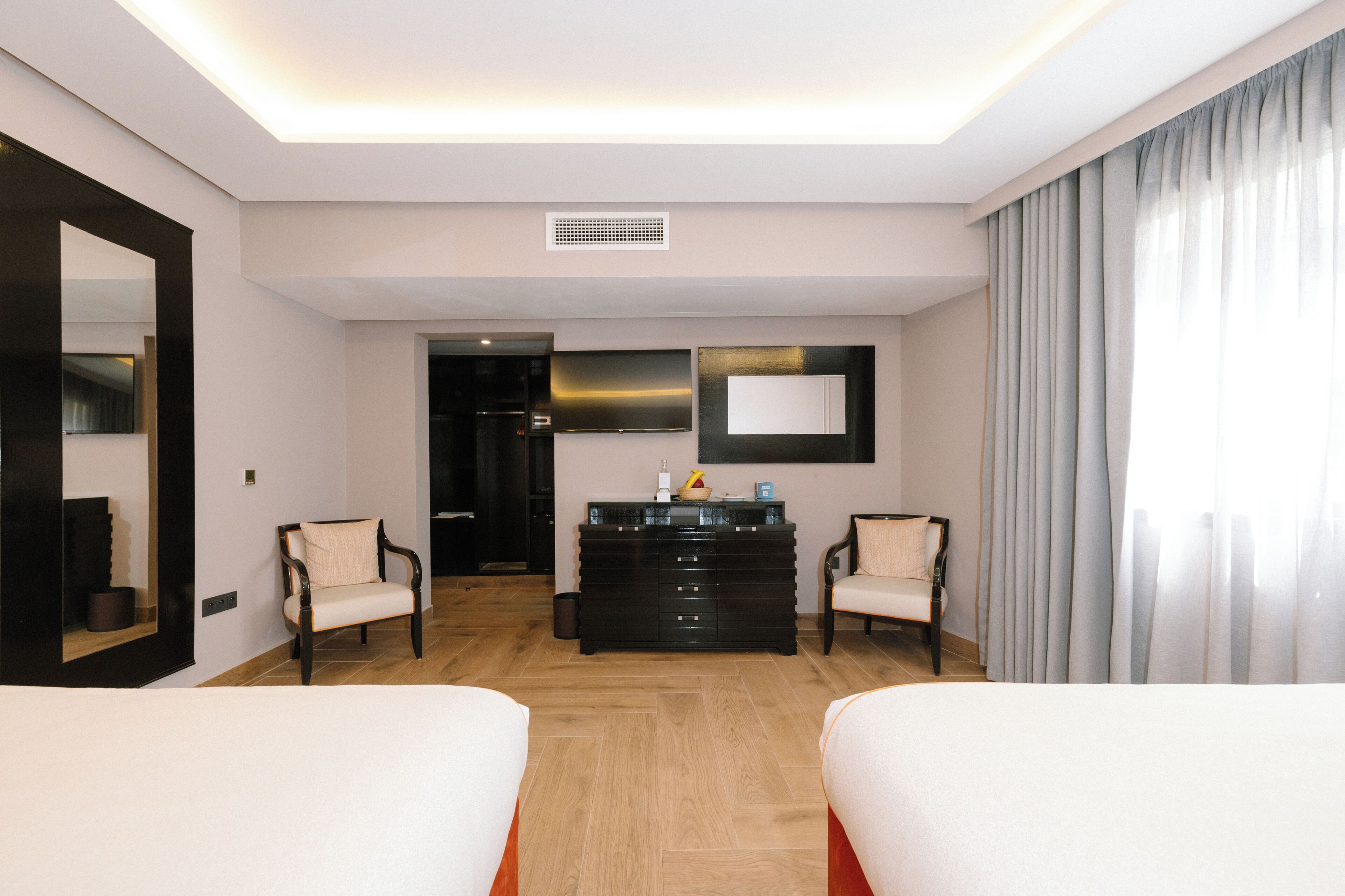A hotel room with two beds, a dresser, a mirror, and a window with curtains.
