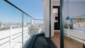 A modern hotel room with a city view, a balcony, and a bed with a headboard.