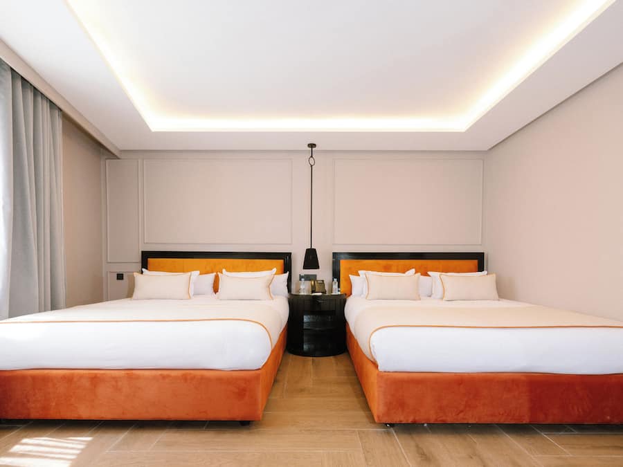 Quarto de hotel com duas camas, uma mesa de cabeceira, um abajur e uma luminária no teto.