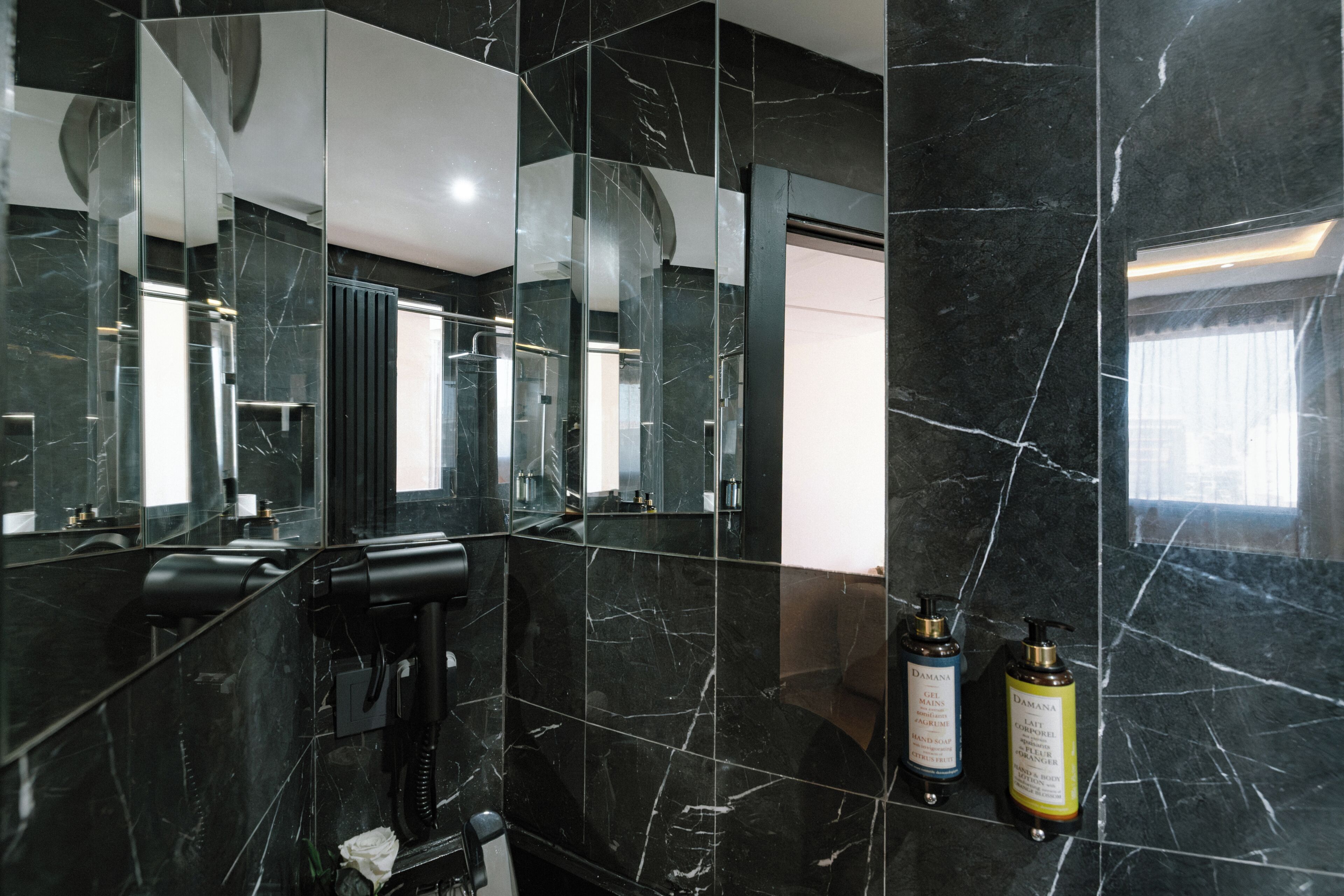 A modern bathroom with black marble walls, a hairdryer, and two bottles of shampoo.