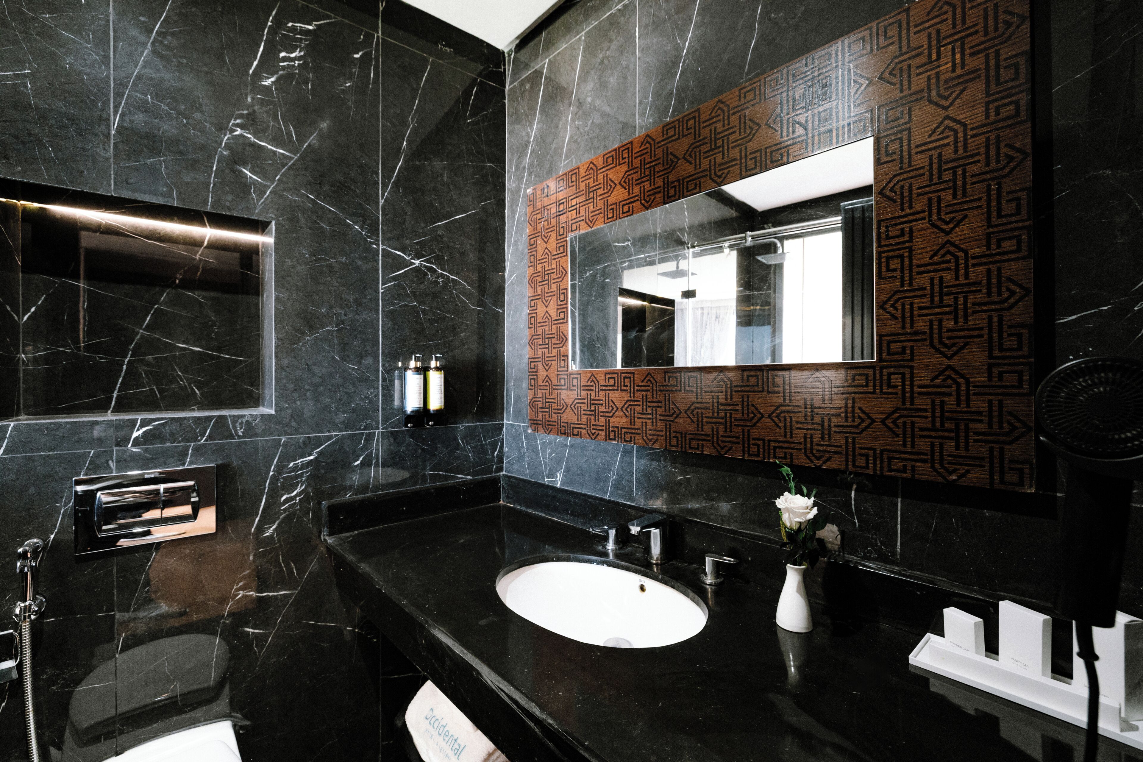 Un baño moderno con lavabo de mármol negro, un espejo de diseño geométrico y un perchero para toallas.