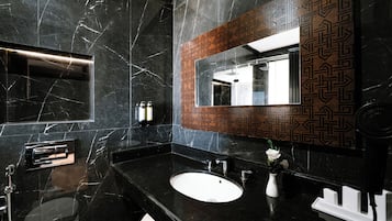 Un bagno moderno con un lavabo in marmo nero, uno specchio con motivo geometrico e un porta asciugamani.