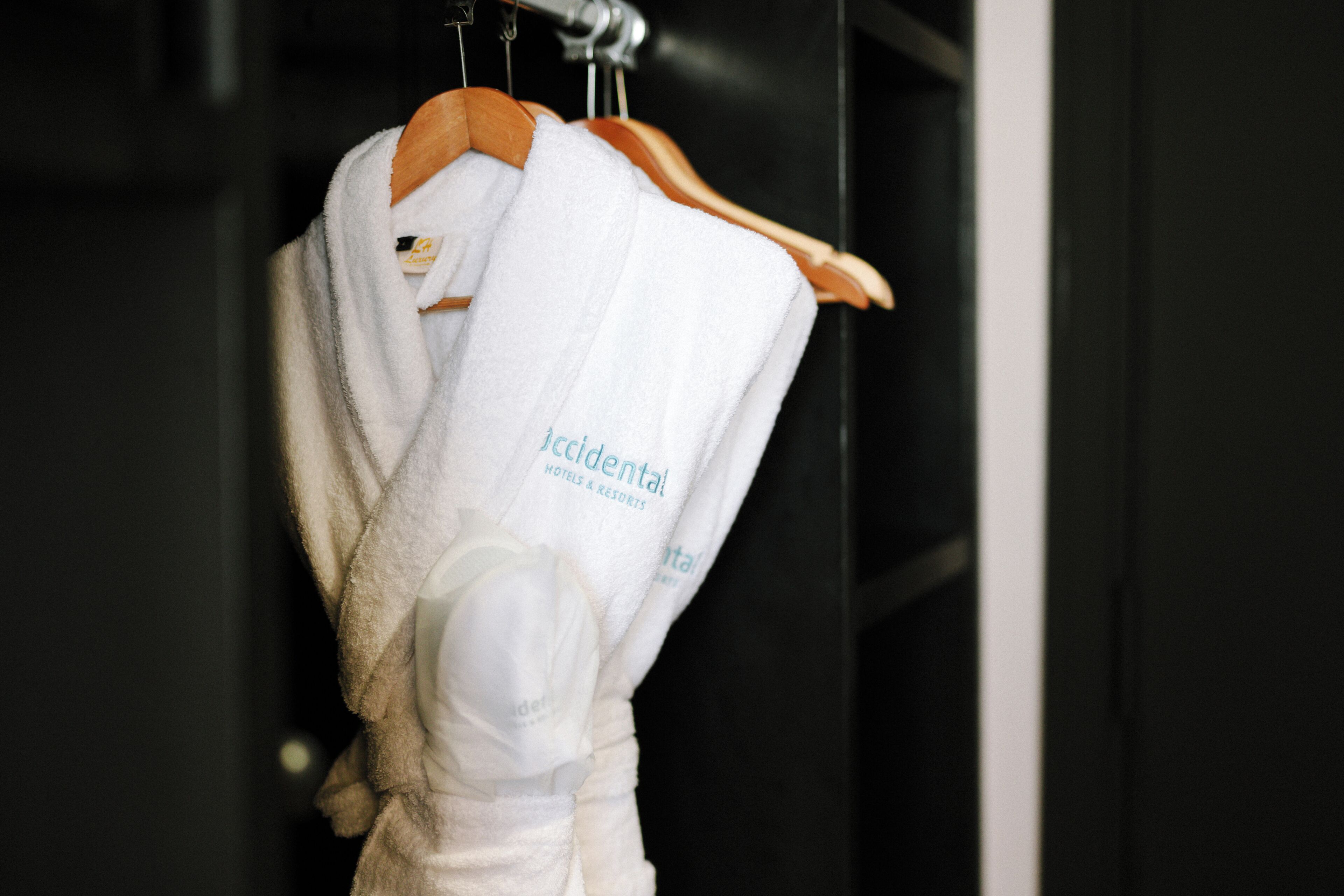 A white robe with 'Accidental Hotels & Resorts' text hanging on a wooden hanger.