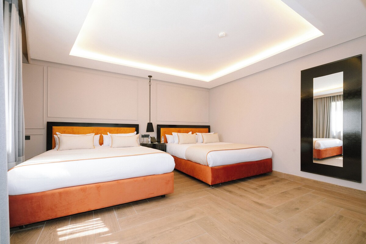 Habitación de hotel con dos camas, un espejo grande y una lámpara en el techo.