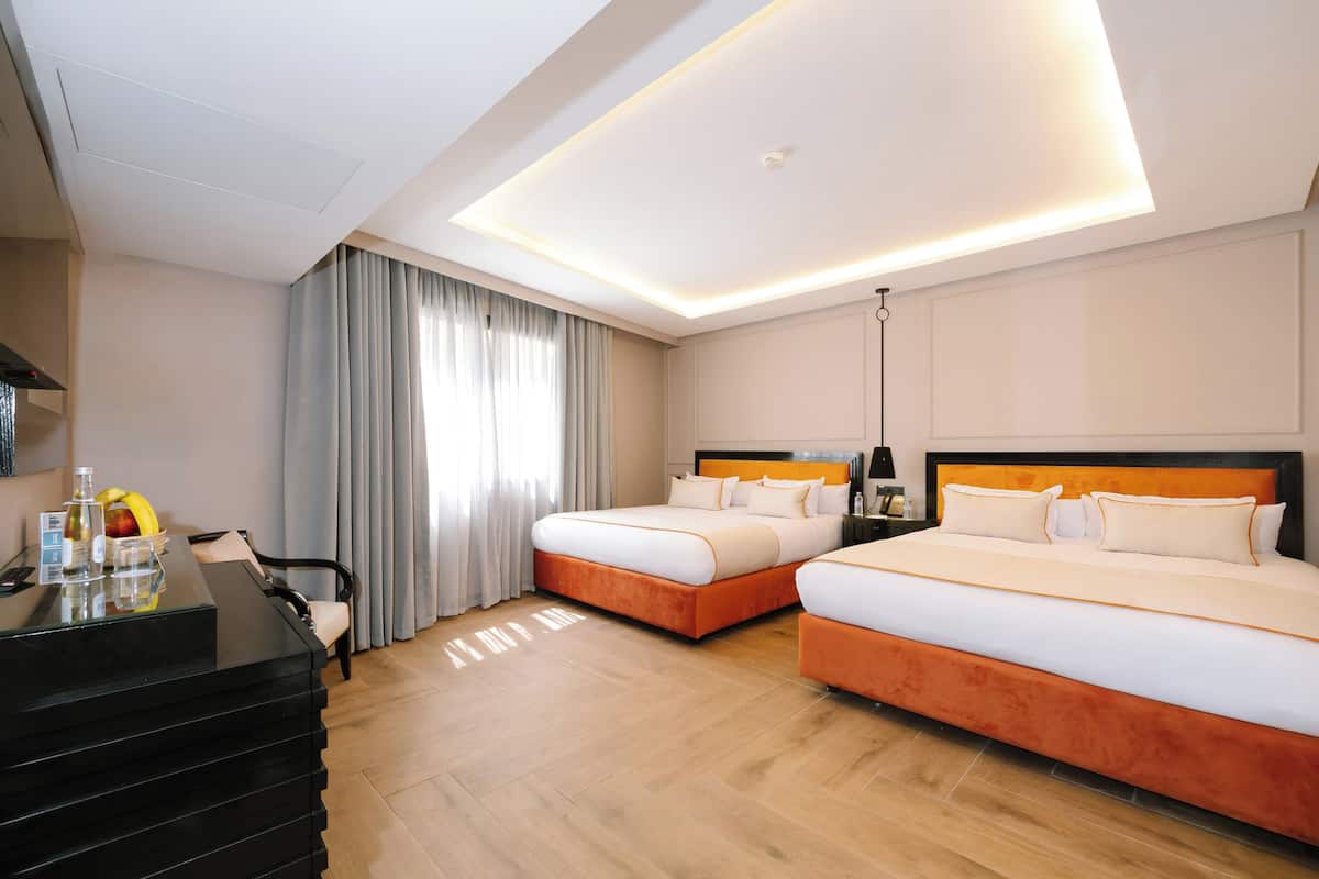 Habitación de hotel con dos camas, un escritorio con silla, televisión y ventana con cortinas.