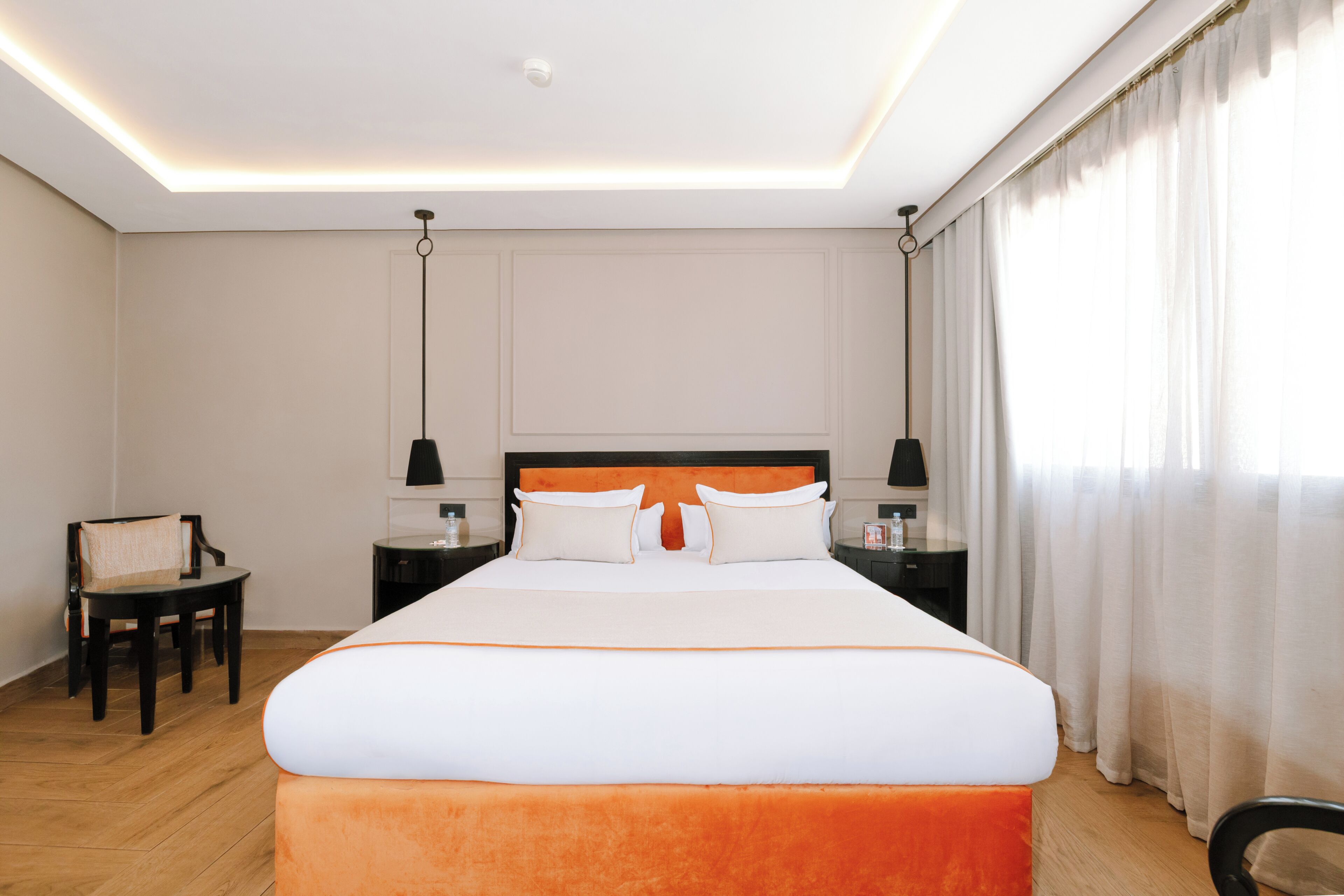 Habitación de hotel con una cama grande, dos mesitas de noche, una silla y una lámpara en el techo.