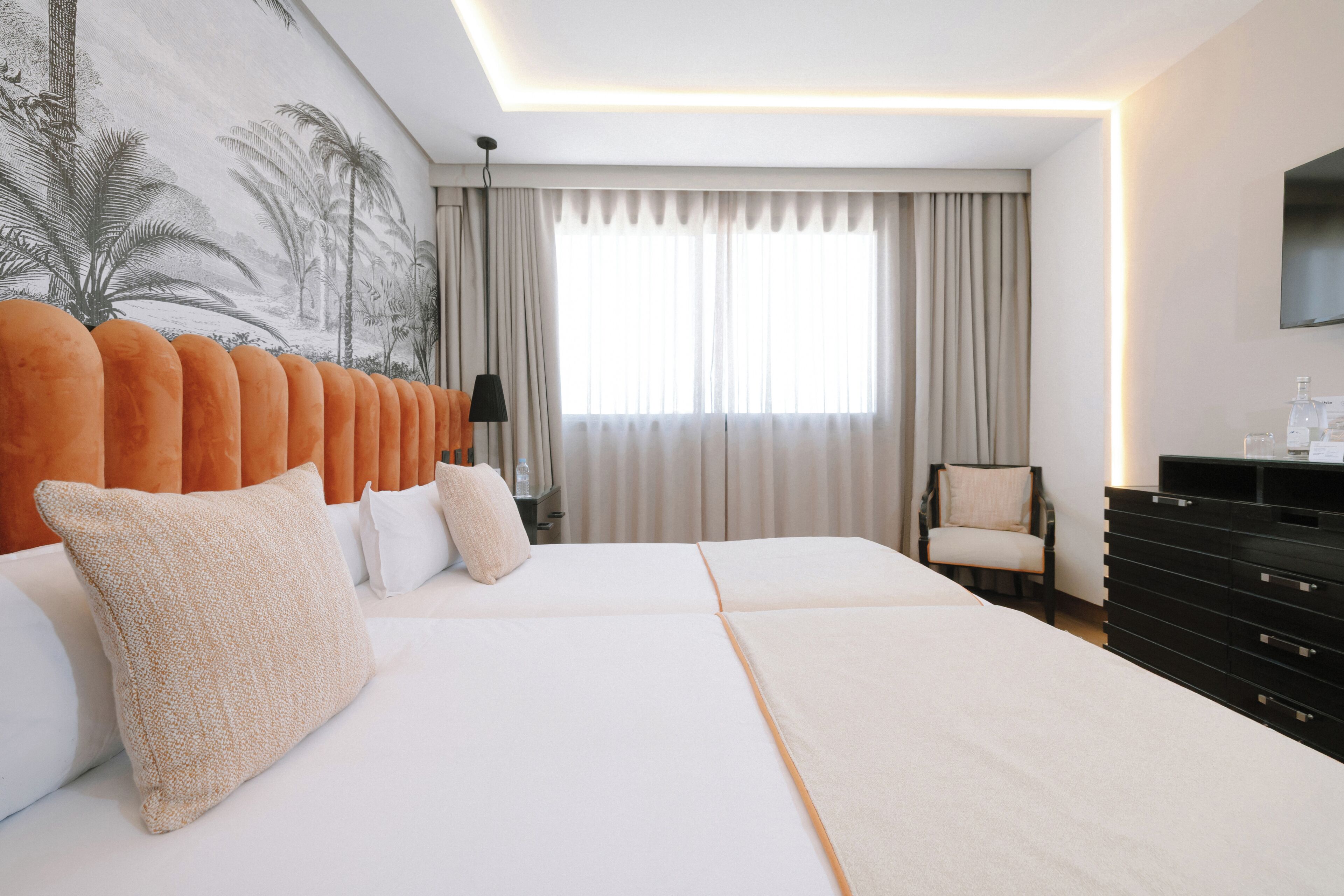 Una habitación de hotel con una cama grande, una silla, un aparador y un televisor en la pared.