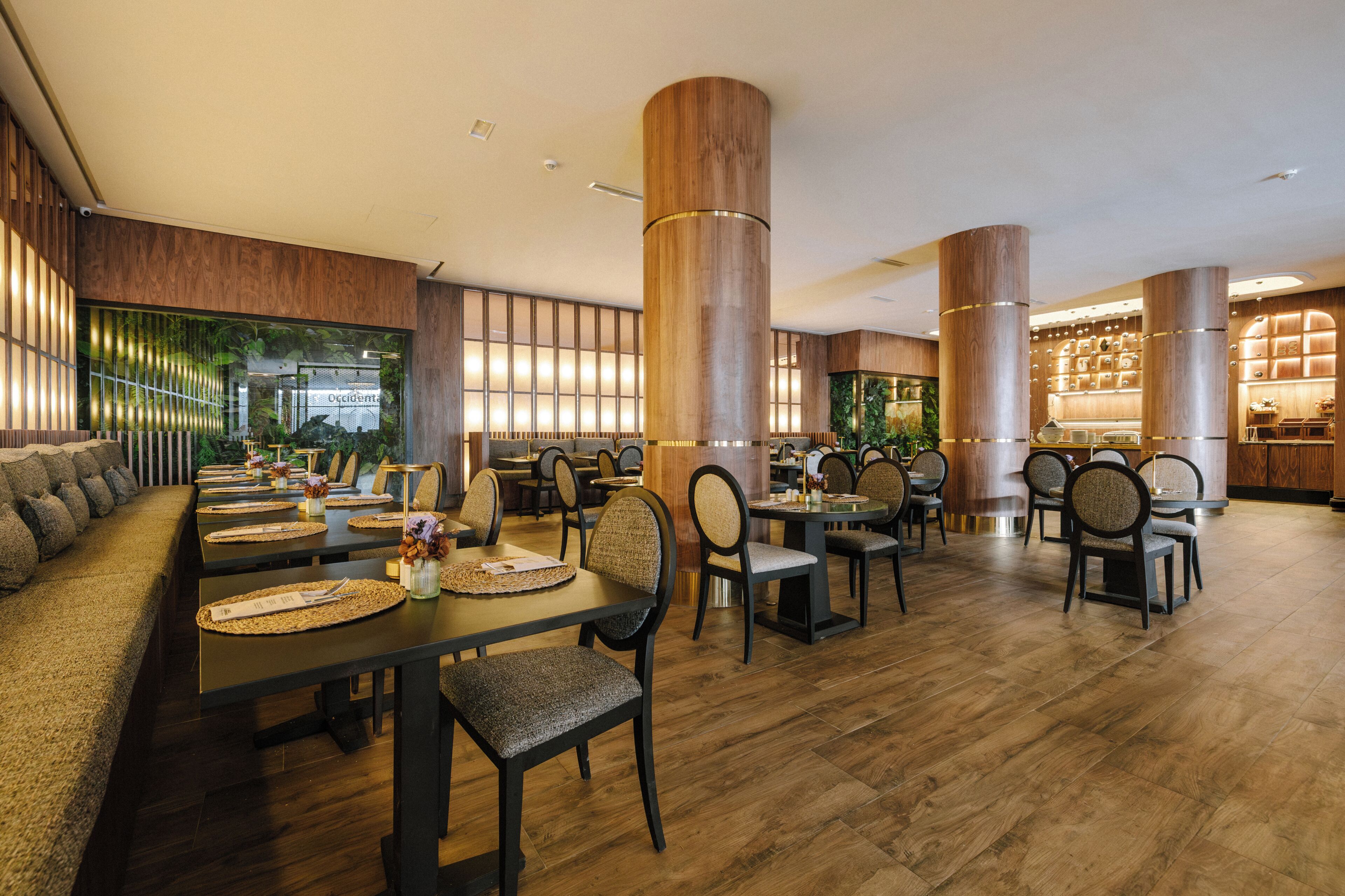 Um restaurante com chão de madeira, altos pilares de madeira e diversos tipos de assentos, incluindo mesas e cadeiras.