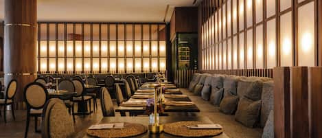 A restaurant with long tables, chairs, and a seating area with cushions.