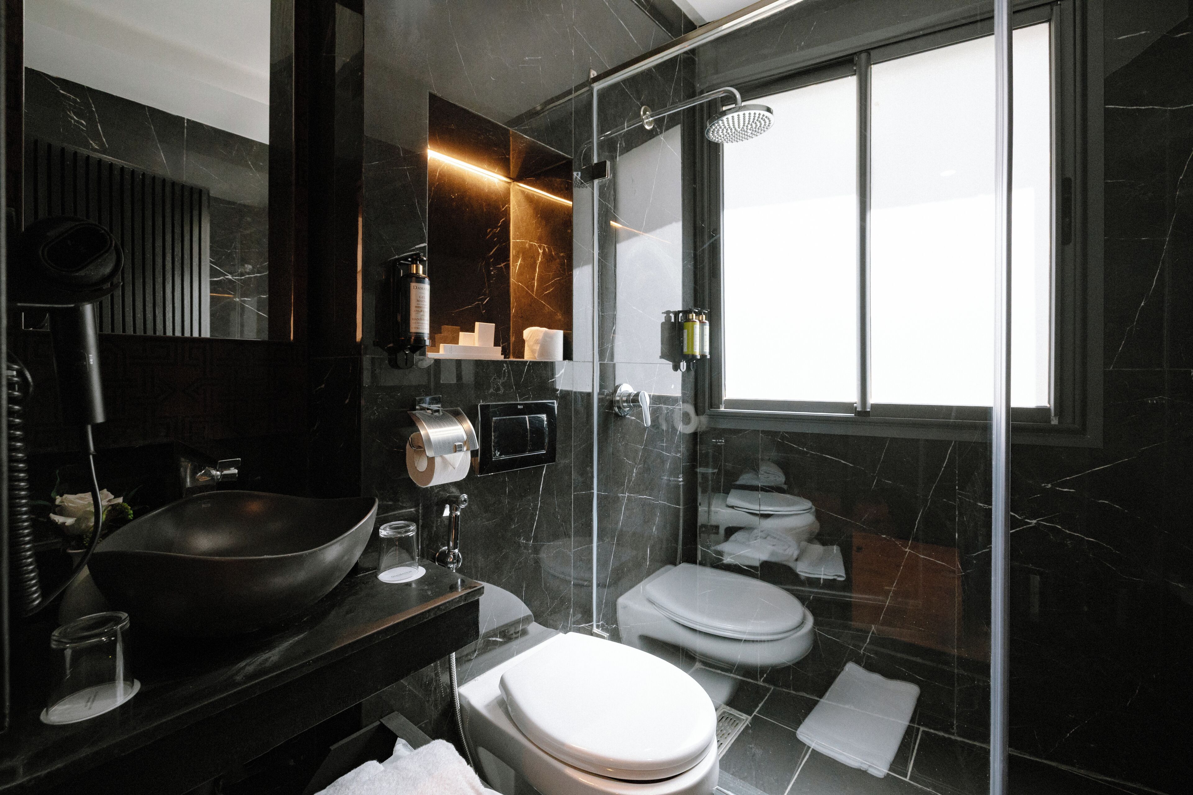 A modern bathroom with a large black basin, a toilet, and a glass-enclosed shower area.